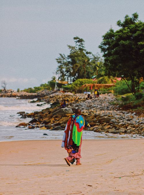 Free A person in vibrant traditional attire walks along a beach in Lagos, Nigeria. Stock Photo