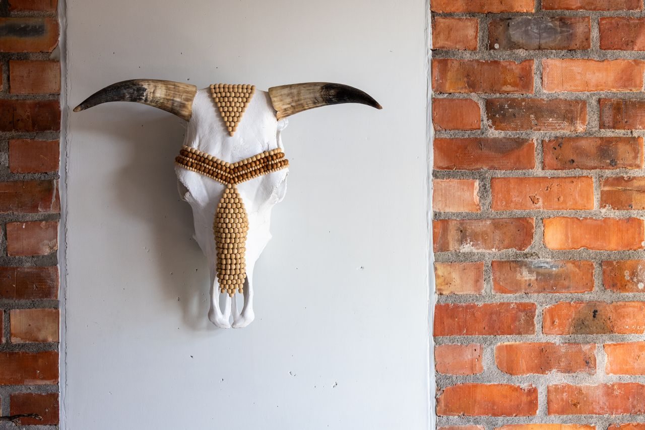 Decorative bull skull with wooden beadwork mounted on a white and brick wall