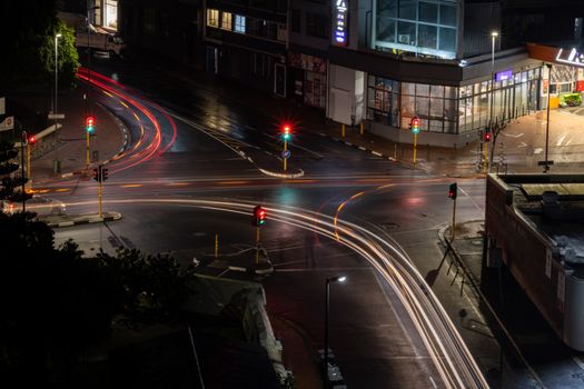 An aerial view of an illuminated city intersection at night, showcasing vibrant light trails from passing vehicles.
