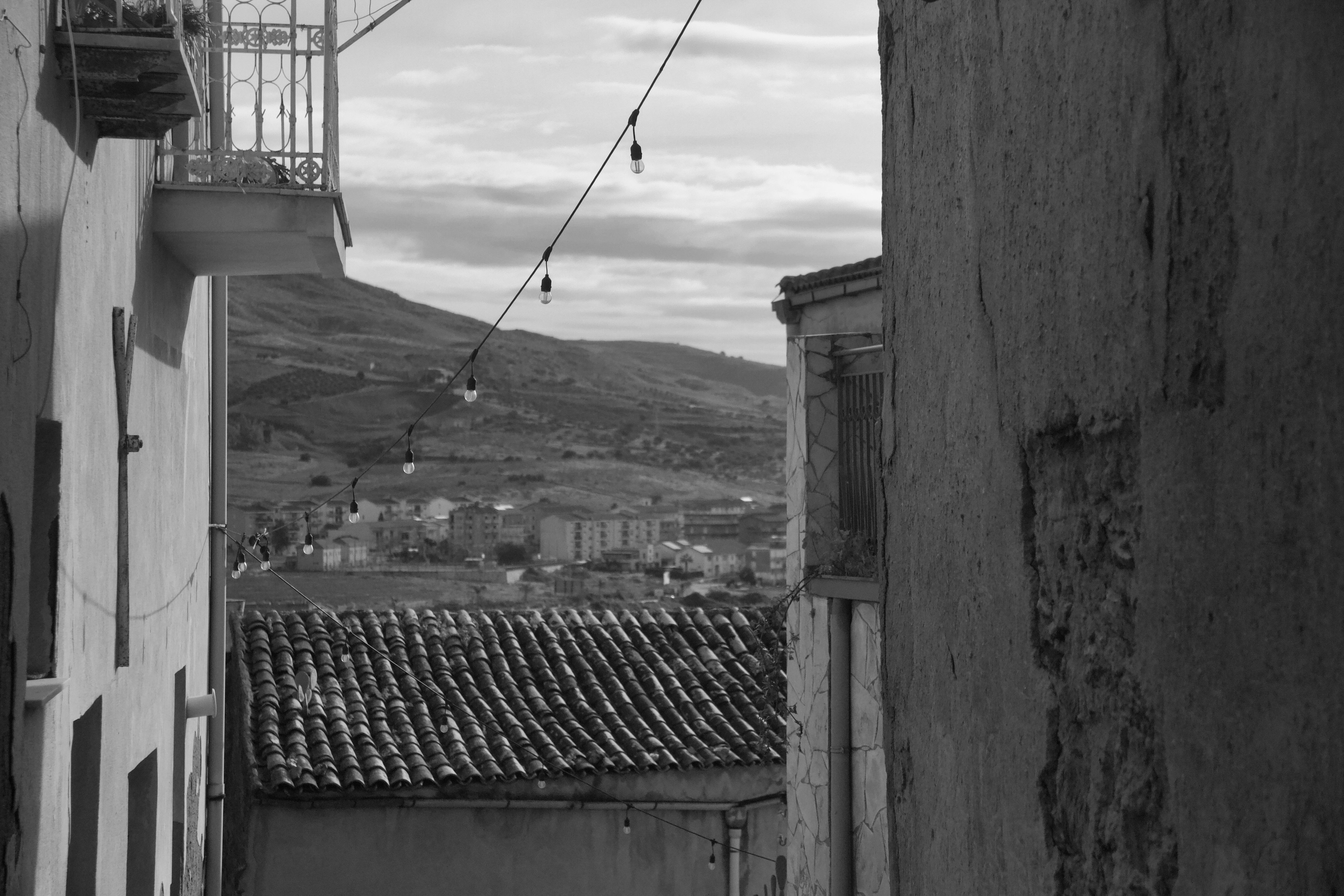 Black and white view of Sicilian alleyway with hillside backdrop, capturing timeless charm.