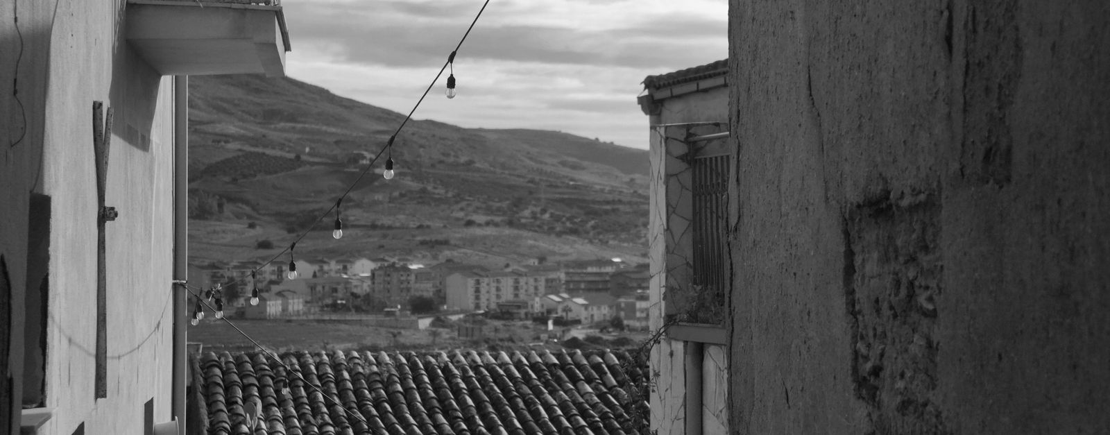 Black and white view of Sicilian alleyway with hillside backdrop, capturing timeless charm.