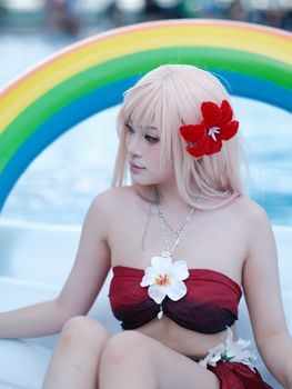 A young woman with flowers poses in a pool with a rainbow float.