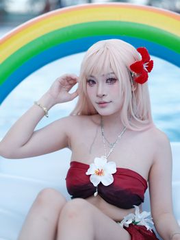 A woman in cosplay attire against a rainbow pool float backdrop, evoking a playful summery feel.