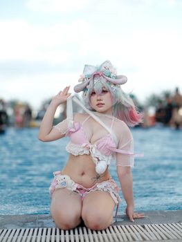 A colorful cosplay character poses poolside in a fantasy-themed costume.