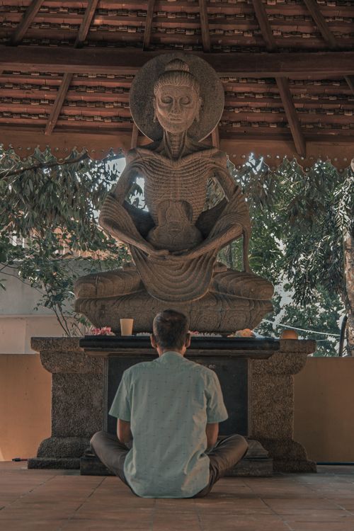 Free Man sitting in meditation before a historic Buddhist statue in Peliyagoda, Sri Lanka. Stock Photo