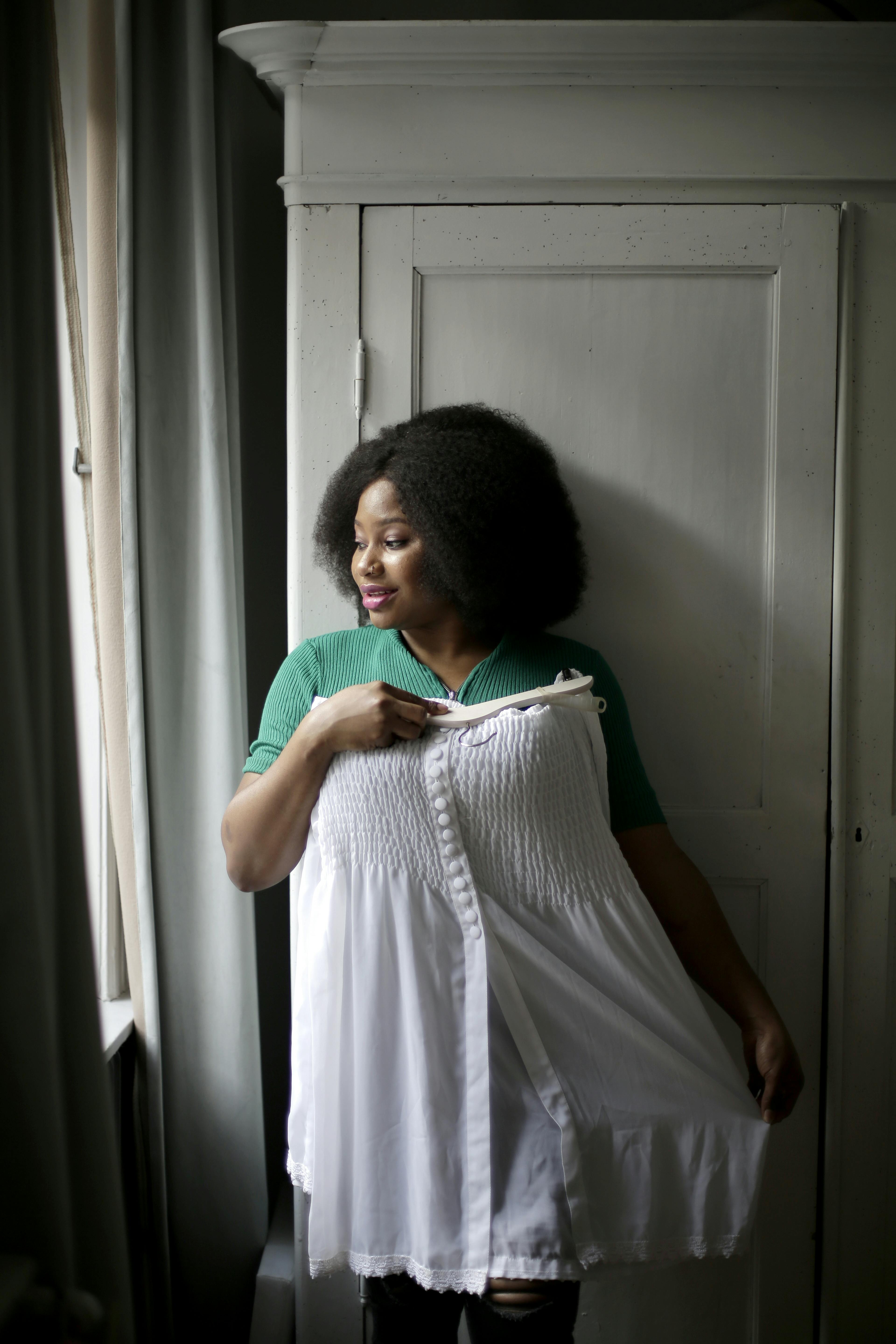 Black woman in green top holds a white dress in an indoor setting.