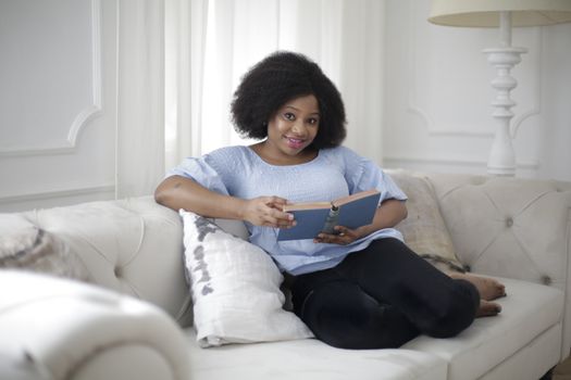 A woman relaxing on a sofa with a book in a bright, calm living room