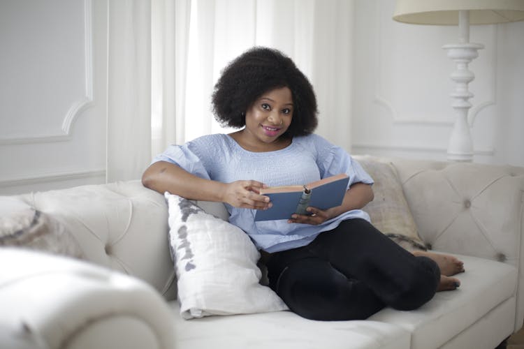 Woman In Blue Shirt And Black Pants Sitting On White Couch