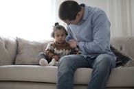 父亲慈爱地将孩子抱到沙发上，捕捉到室内为人父母的温柔时刻