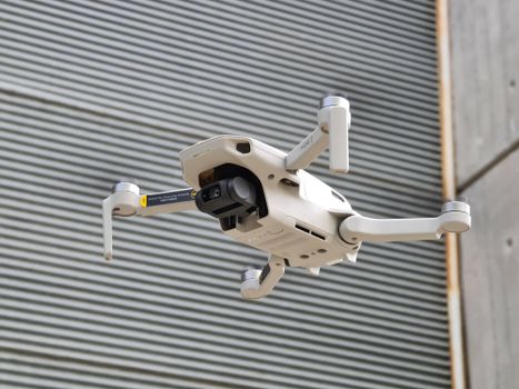 A compact camera drone hovering outdoors with a modern industrial backdrop.