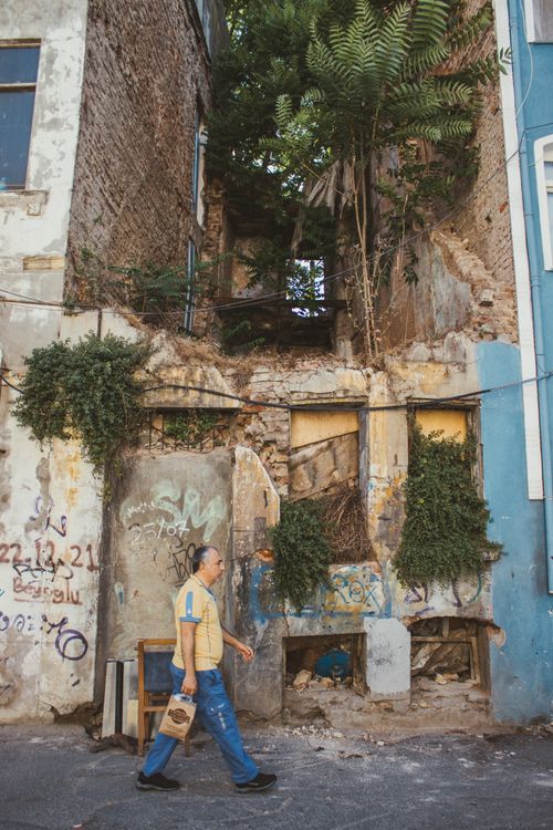 Free A man walks by a dilapidated, graffiti-covered building with overgrown vegetation. Stock Photo