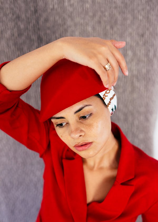 From above of young thoughtful female wearing retro hat and red jacket looking away in studio on gray background
