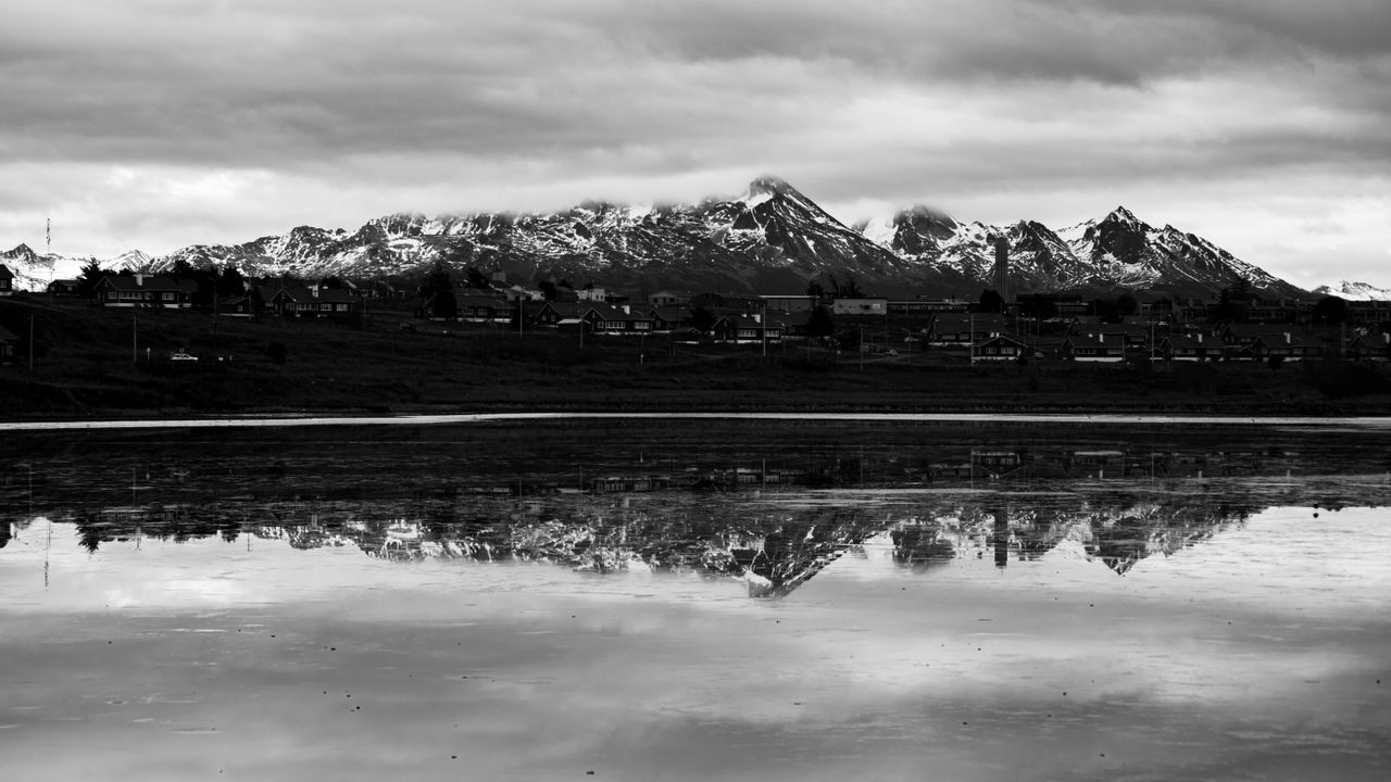 black and white photo of mountains reflecting in water in ushuaia arge