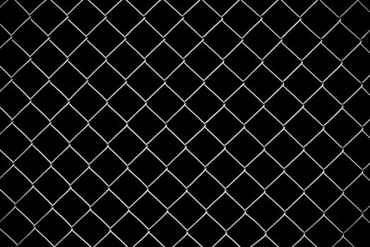 Black and white image of a chain-link fence forming a diamond pattern against a dark background.