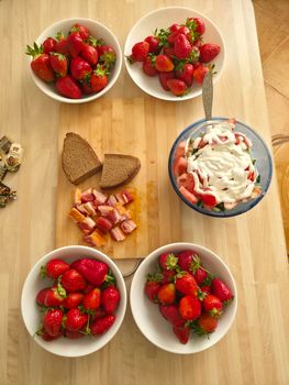 Aerial view of fresh strawberries, bread, and cream in bowls on a wooden table, perfect for breakfast.