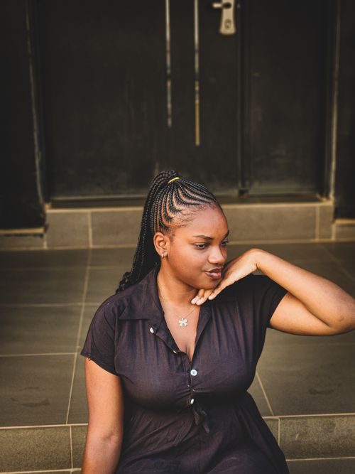 Free Portrait of a confident young woman with braided hair sitting outdoors in a relaxed pose. Stock Photo