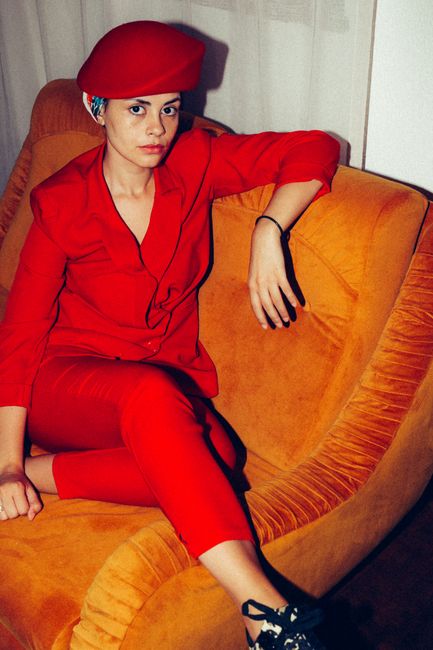A woman in a stylish red outfit leisurely sitting on an orange couch indoors.