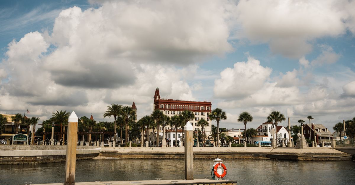Scenic view of St. Augustine's waterfront with historic buildings and palm trees under a cloudy sky.