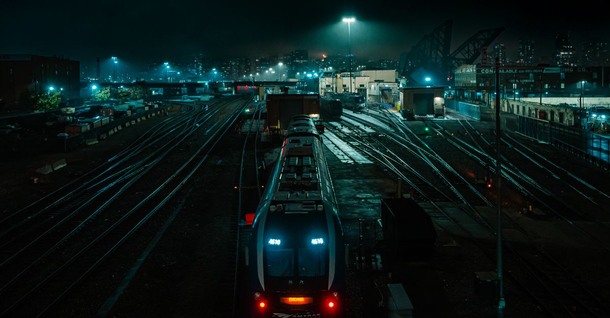 Vivid night view of train yard in Chicago with city skyline, creating a moody urban atmosphere.