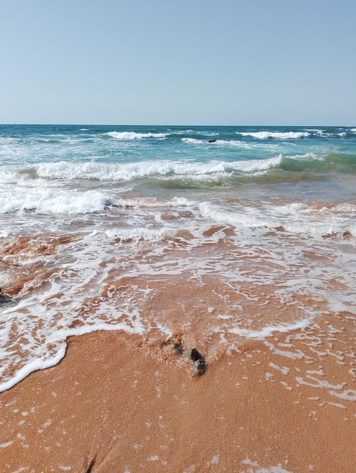 Free Capture of gentle waves lapping a sandy beach under a clear blue sky. Stock Photo
