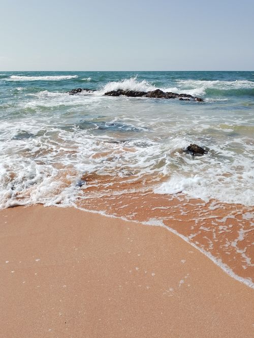 Free Tranquil sandy beach with waves gently hitting rocks on a sunny day. Stock Photo