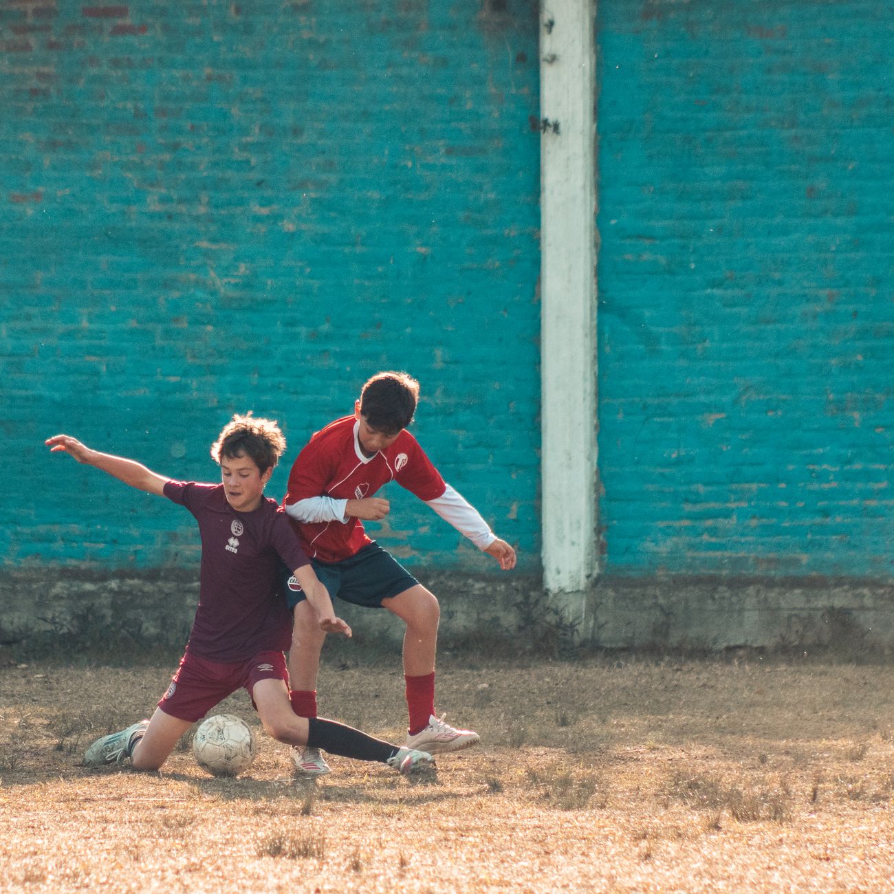 Two amateur footballers performing a pressured passing drill between cones on an outdoor training field