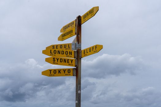 Yellow directional signpost under cloudy skies at Cape Reinga, Northland, NZ.