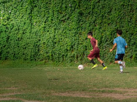 Two teenagers playing soccer against a lush green backdrop on a sunny day.