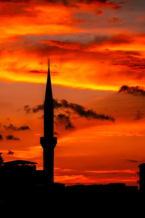 Free A stunning silhouette of a mosque minaret against a vivid orange and red sunset. Perfect for travel and cultural themes. Stock Photo