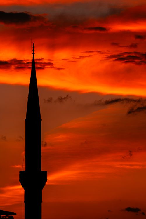 Free A dramatic silhouette of a minaret against a vivid orange and red sunset sky. Stock Photo