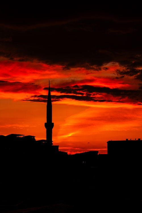 Free Silhouette of a mosque minaret against a vibrant red sunset sky, creating a dramatic cityscape. Stock Photo