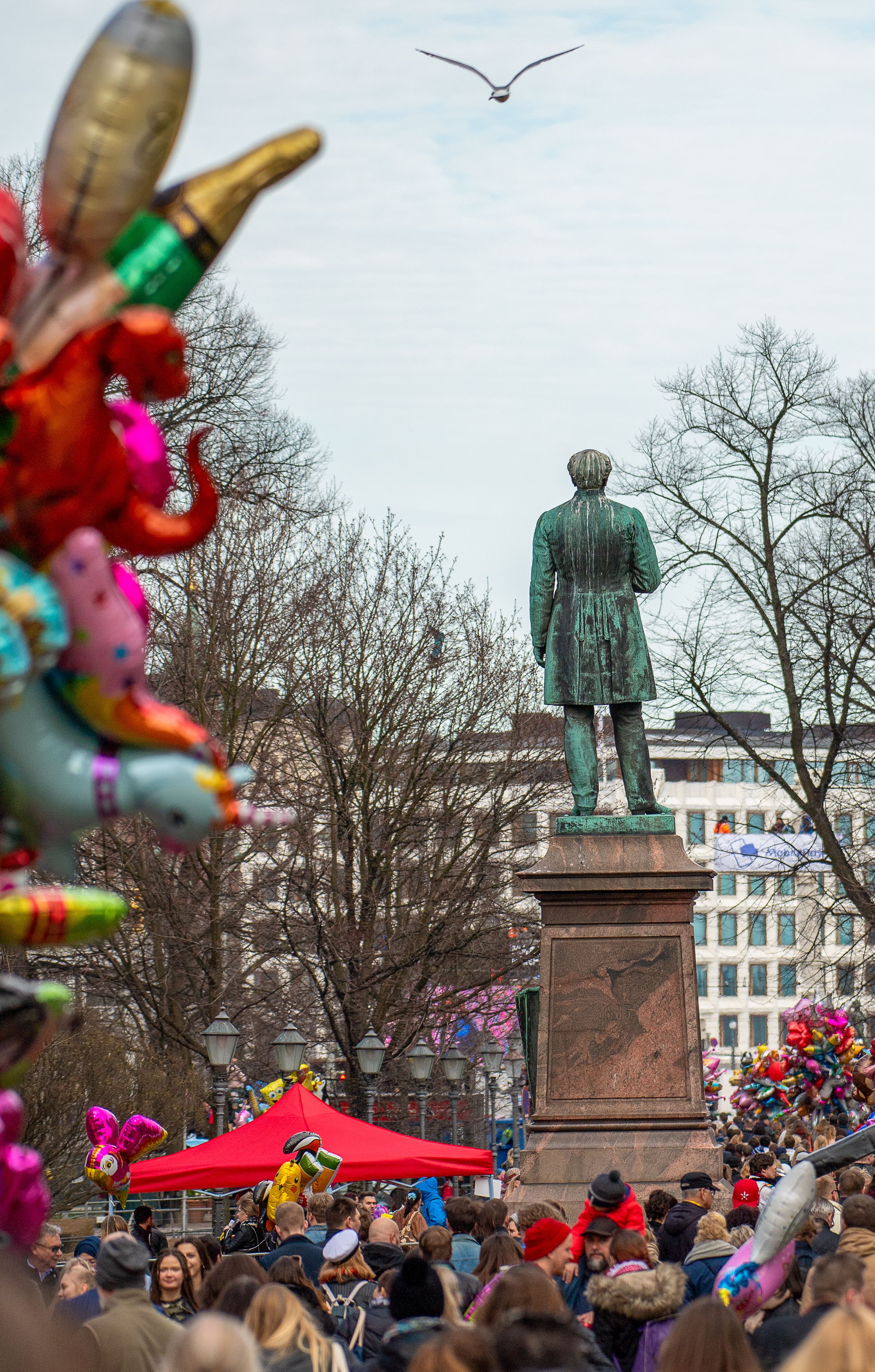 Festive May Day event in Helsinki's park with Runeberg's statue surrounded by balloons and crowds.