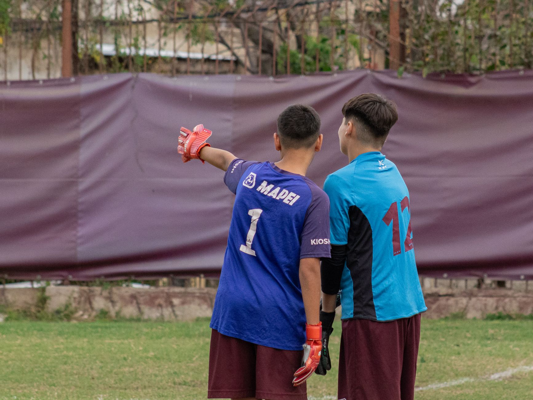 Two young soccer goalkeepers in uniforms planning during practice outdoors.