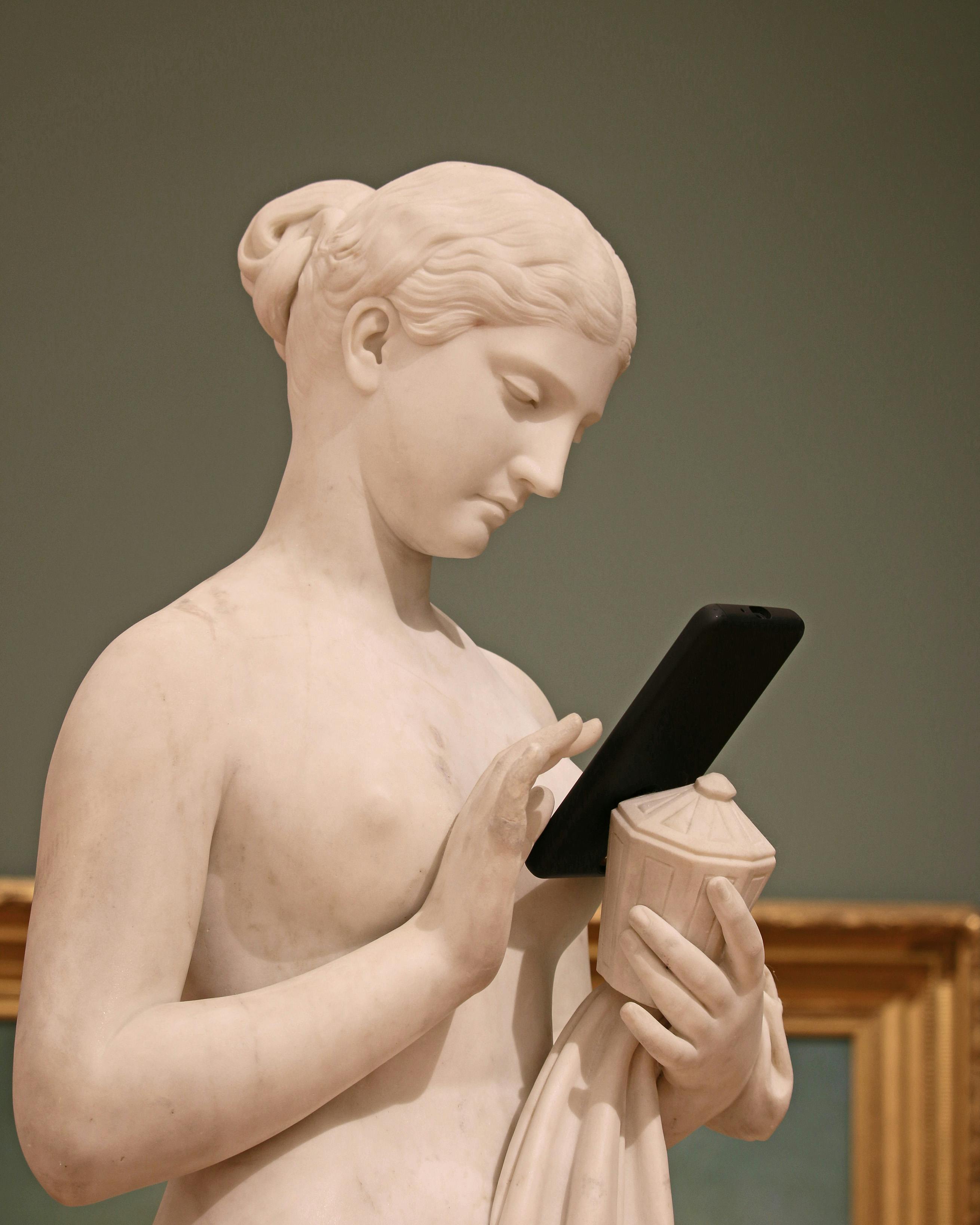 classic female statue surfing internet on smartphone in museum