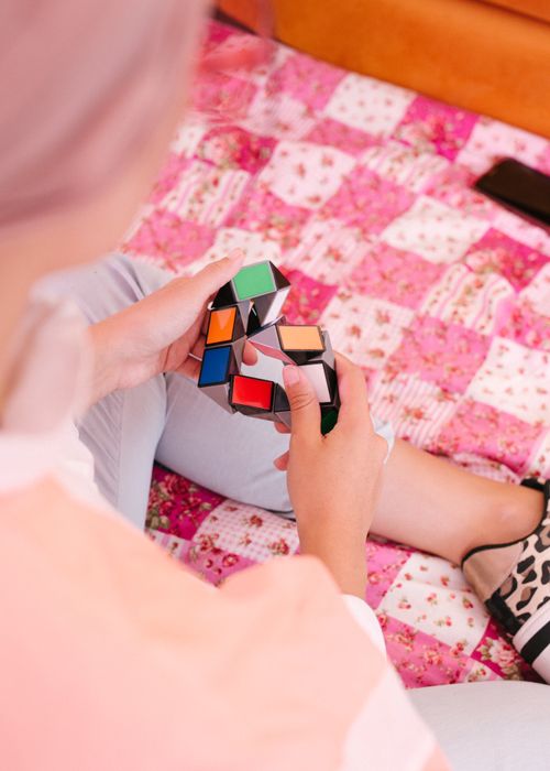 Free From above back view of female in trendy wear sitting on cozy bed and entertaining with colorful plastic toy while relaxing during weekend at home Stock Photo