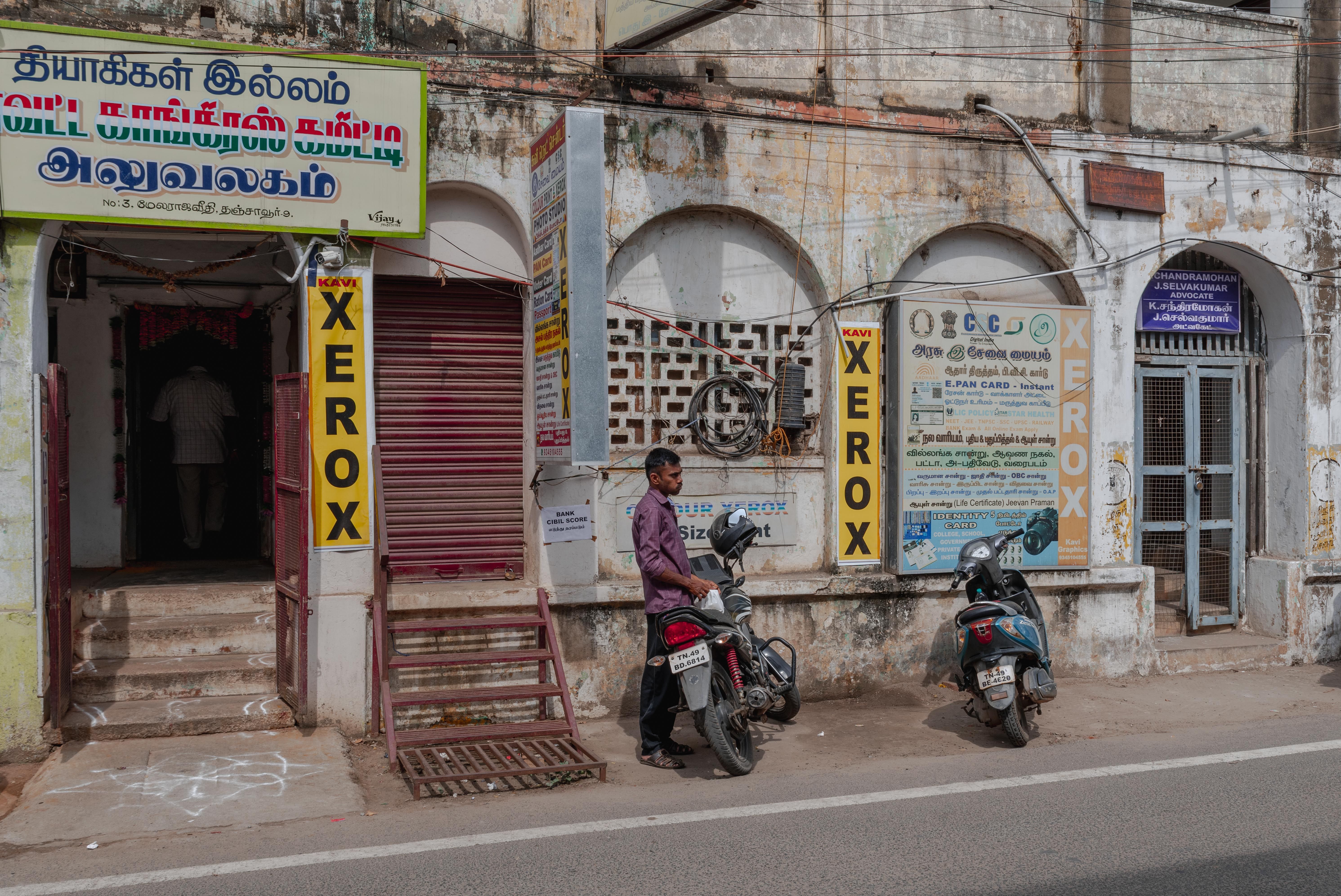 Street view in Tanjore, Tamil Nadu with people and scooters in front of shops.