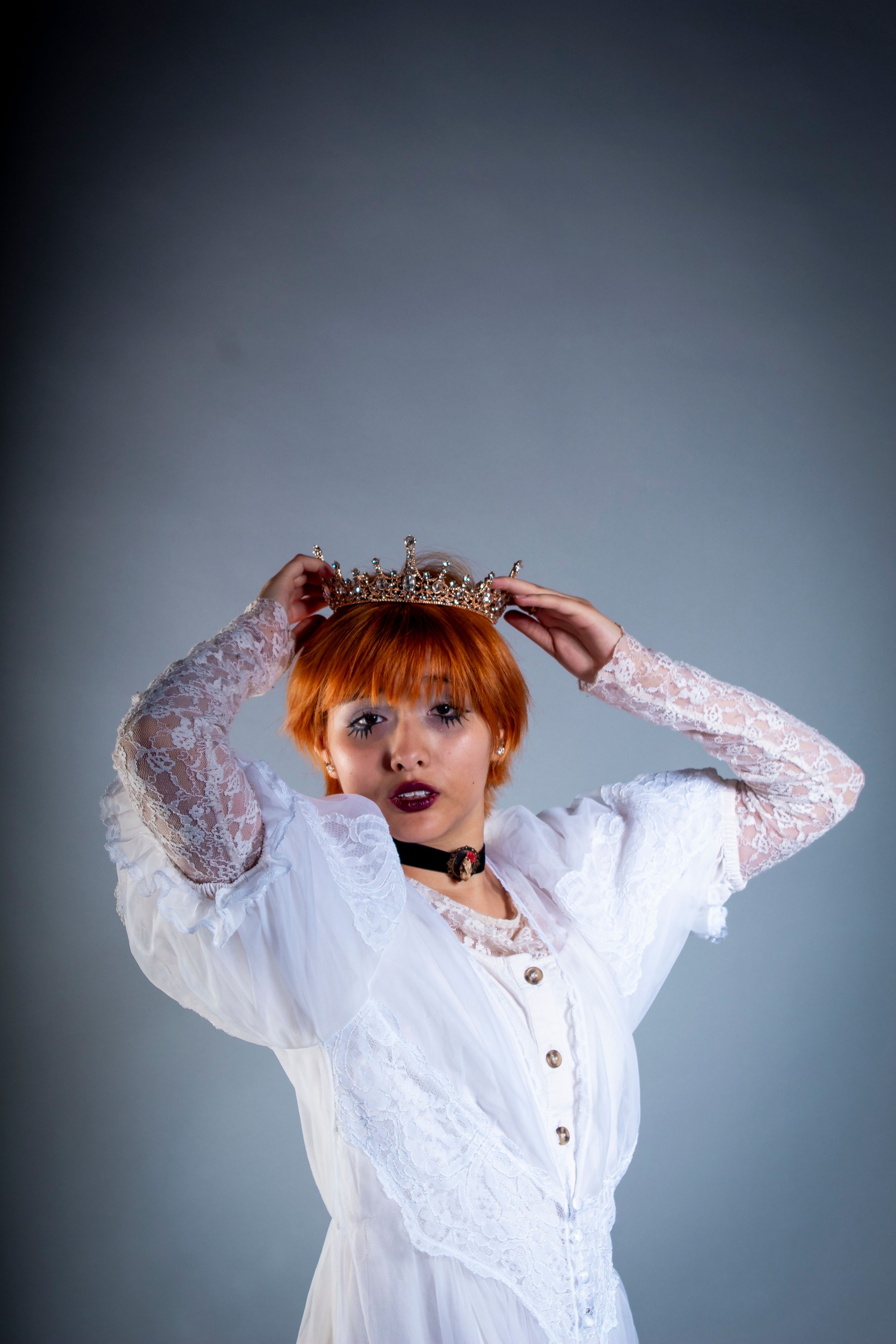 Sophisticated portrait of a woman in Victorian attire adjusting a crown.
