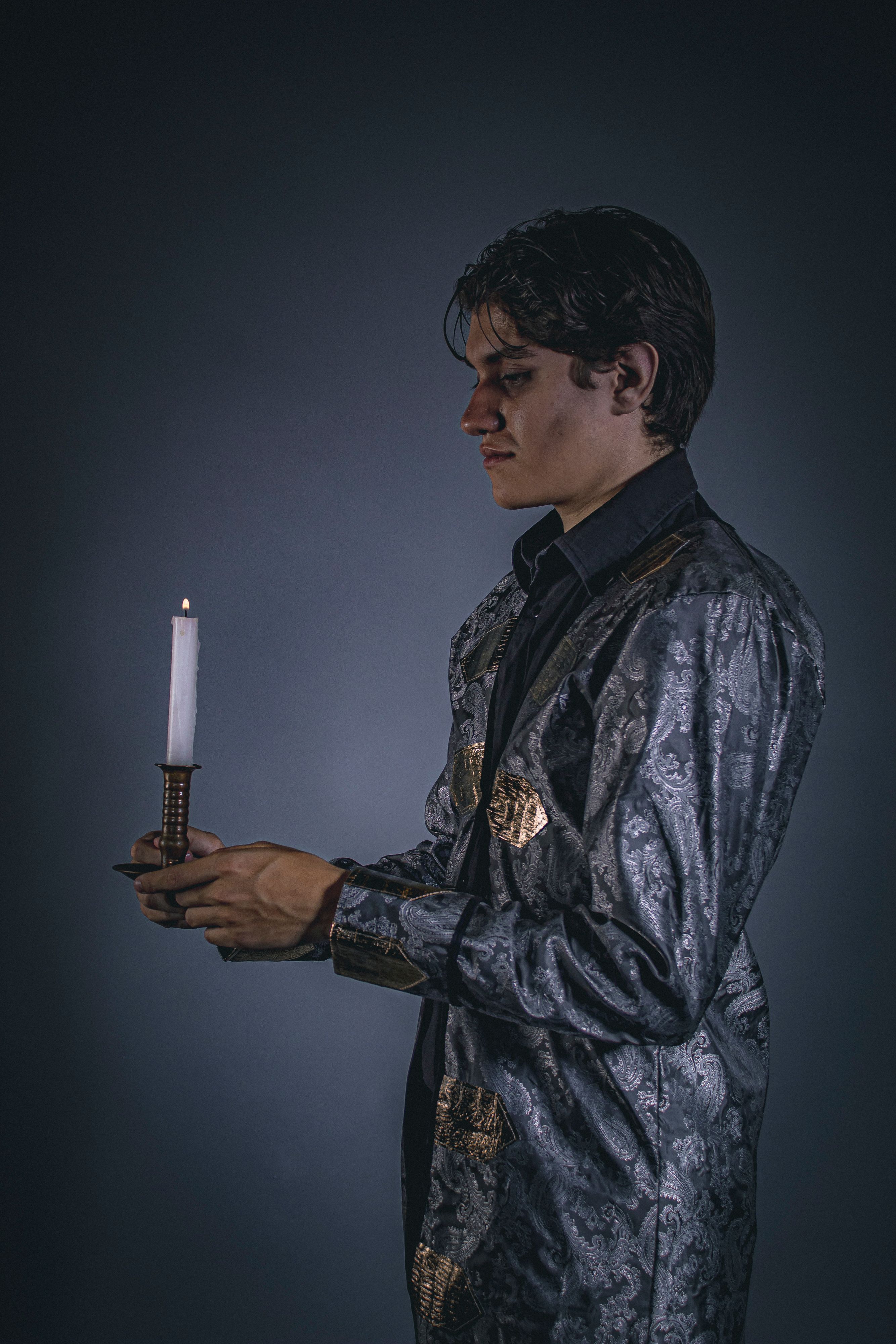 A young man in Victorian attire holding a candle, creating a moody, dramatic atmosphere.