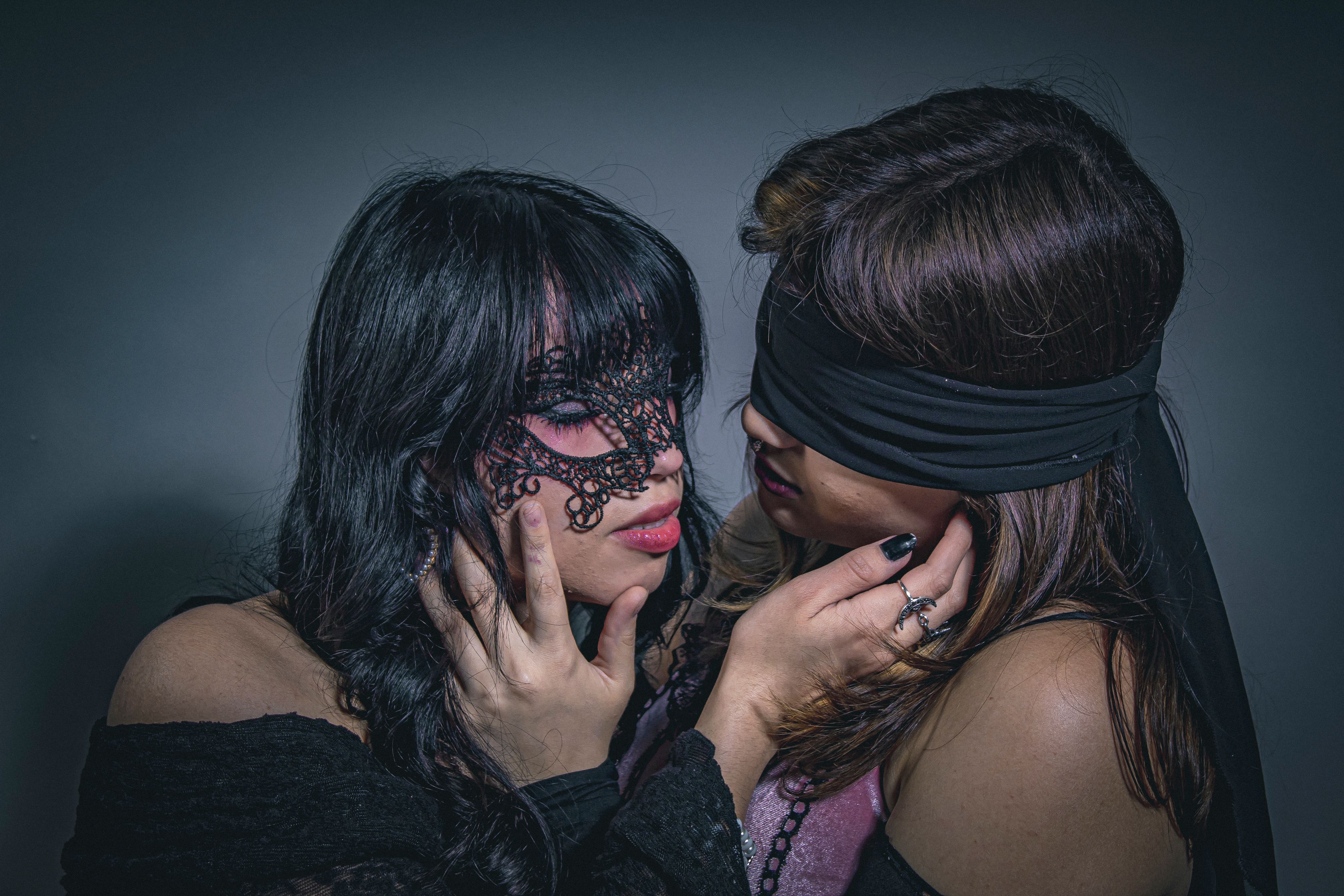 Two women engaged in an intimate pose wearing masks, creating a mysterious and dramatic effect.