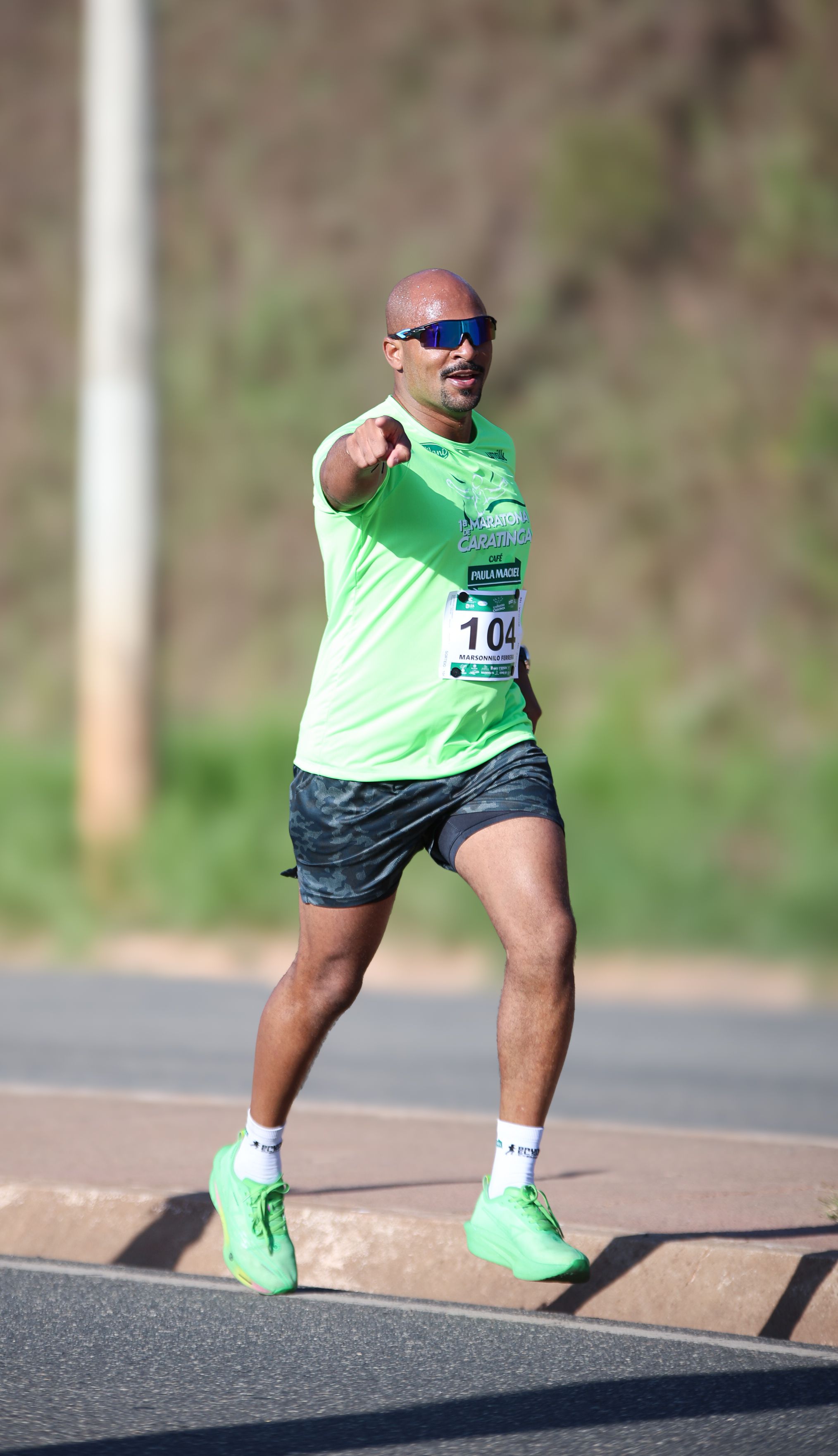 A man confidently running a marathon outdoors, pointing towards the camera with a smile.