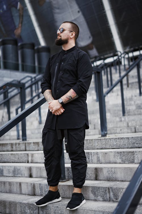 黑色衬衫和黑色裤子，站在灰色的混凝土楼梯上的男人