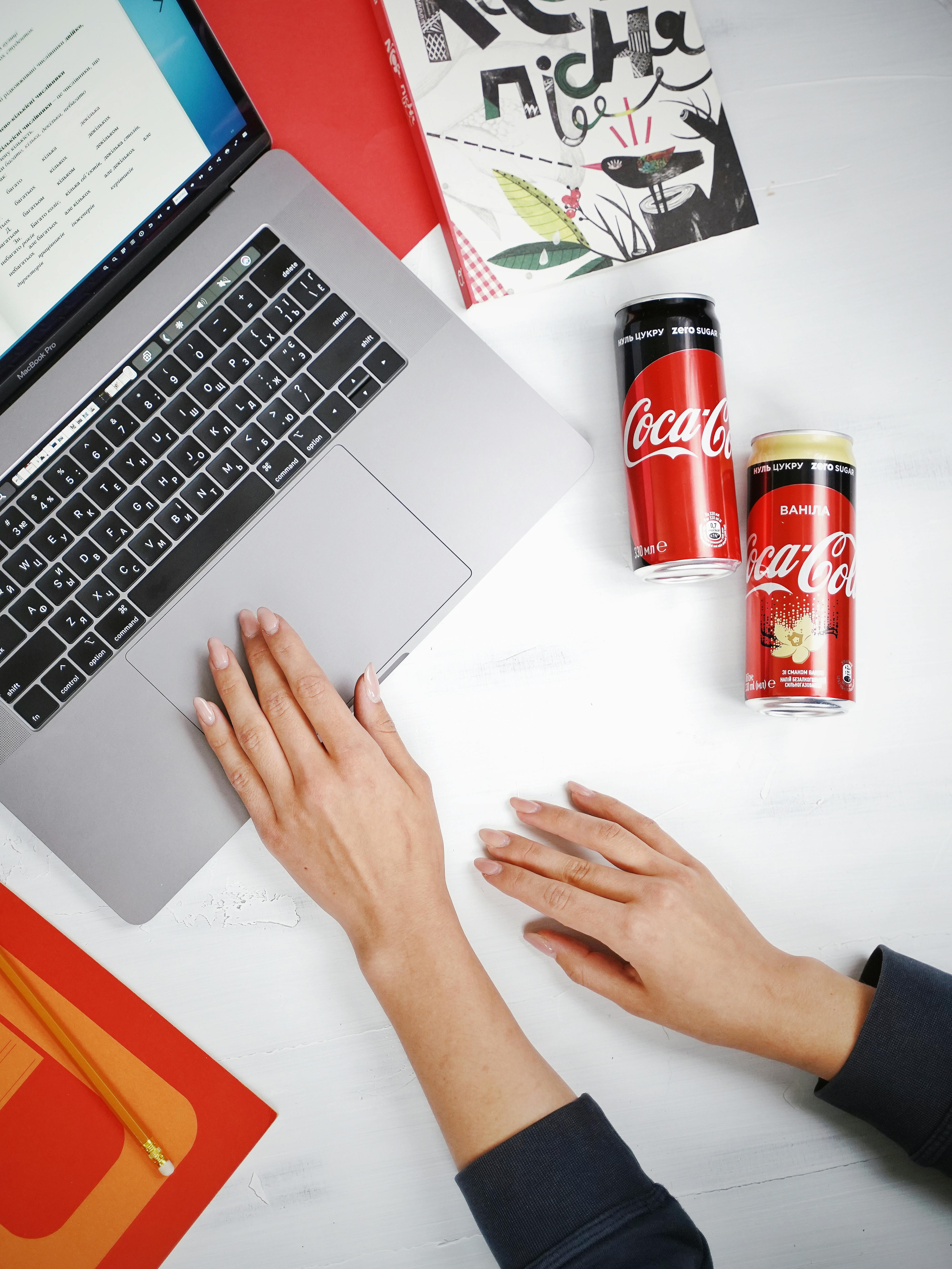 Person Using Macbook Pro Beside Coca Cola Cans - Hotcopy