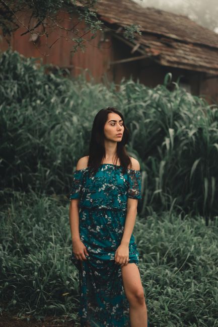 A woman in an off-shoulder floral dress stands confidently outdoors, surrounded by lush greenery.