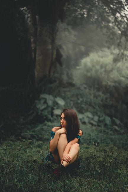 A solitary woman sits contemplatively in a tranquil, misty forest setting.
