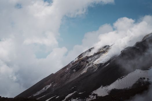 Stunning capture of Mount Etna releasing steam and smoke under a cloudy sky.