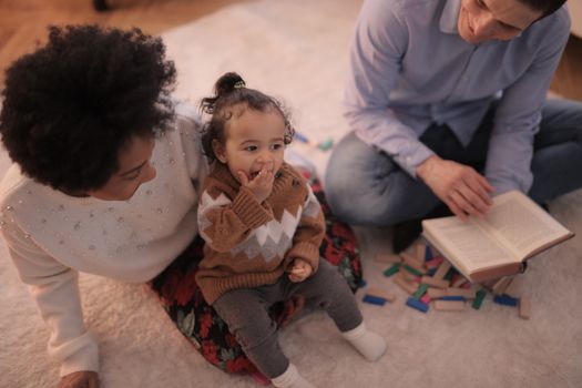 A family of three enjoying quality time playing and reading together in a warm indoor setting.