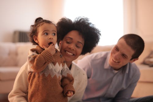 Woman in White Long Sleeve Shirt Carrying Baby in Brown Sweater