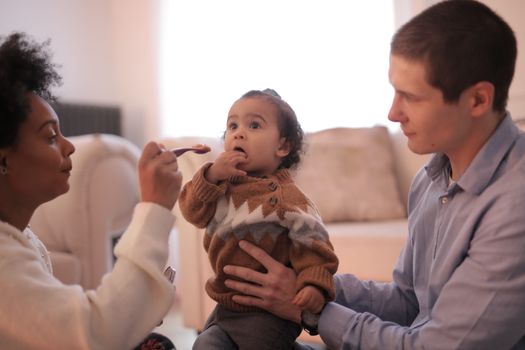 A caring family moment where parents feed their baby in a cozy living room setting.