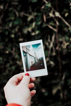 一只修剪整齐的手拿着即时照片，背景是绿色的户外