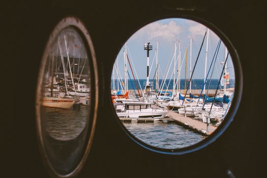 Looking through a porthole at a marina full of sailboats on a clear day.
